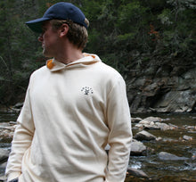 Model wearing cream Ridgeline Hoodie in outdoor setting by a creek – front view