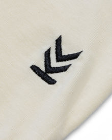 Detail shot of embroidered logo at bottom left hem of cream Wild Tee